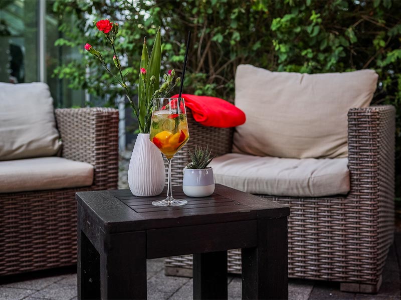 Bequeme Rattansessel mit Kissen um kleinen Tisch mit Cocktail und Pflanzen im Garten.