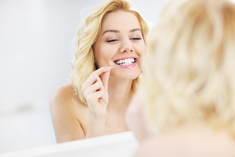 Woman looking at herself in the mirror while she is flossing
