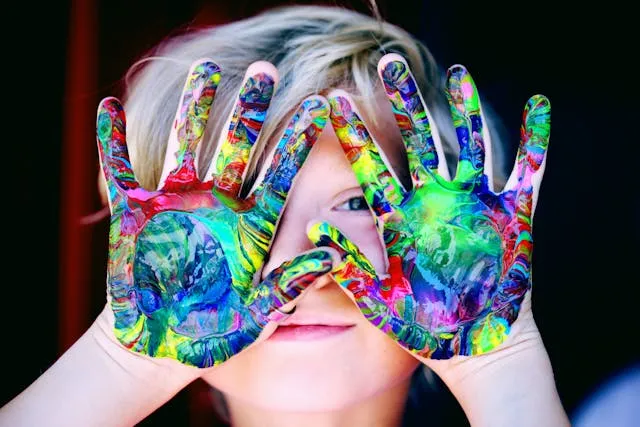 A kid with painted hands smiling and looking at the camera