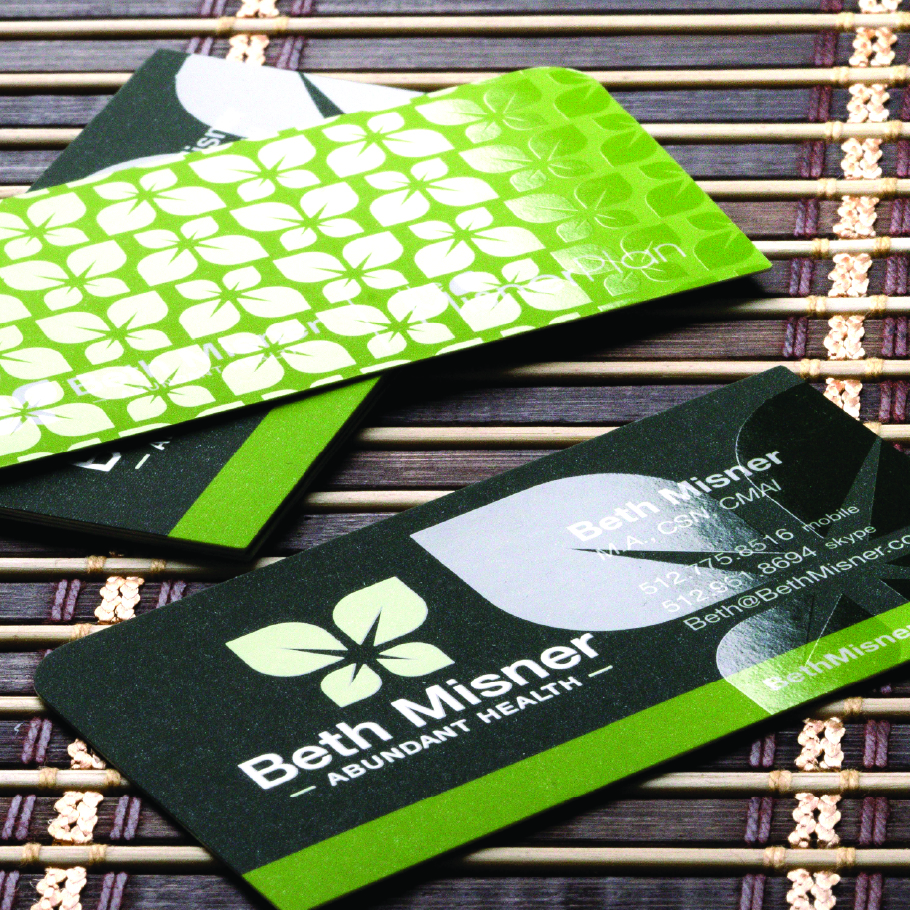 Two green and black business cards for Beth Misner of Abundant Health on a bamboo mat.