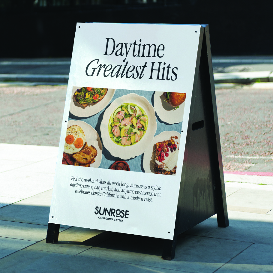 A-frame sign on sidewalk advertising Sunrose California Eatery with images of various meals and text about daytime dining and events.