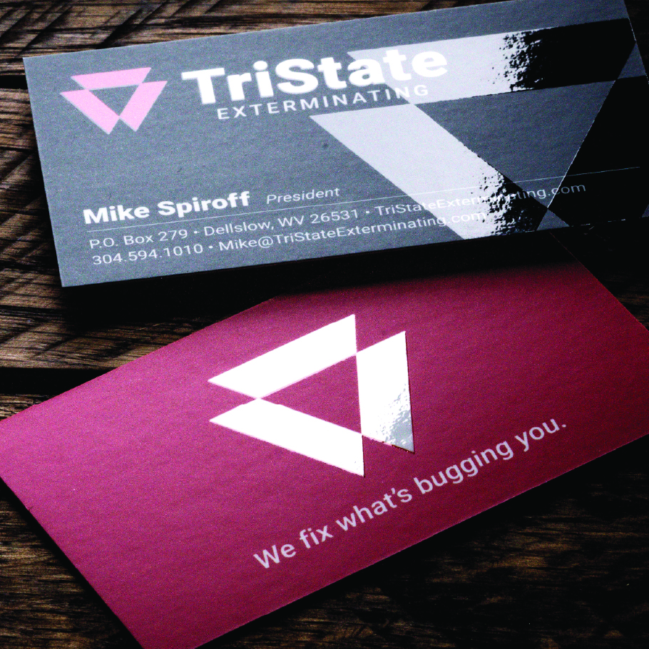 Two TriState Exterminating business cards on a wooden surface, one gray with contact details for Mike Spiroff, President, and one red with the slogan "We fix what's bugging you."