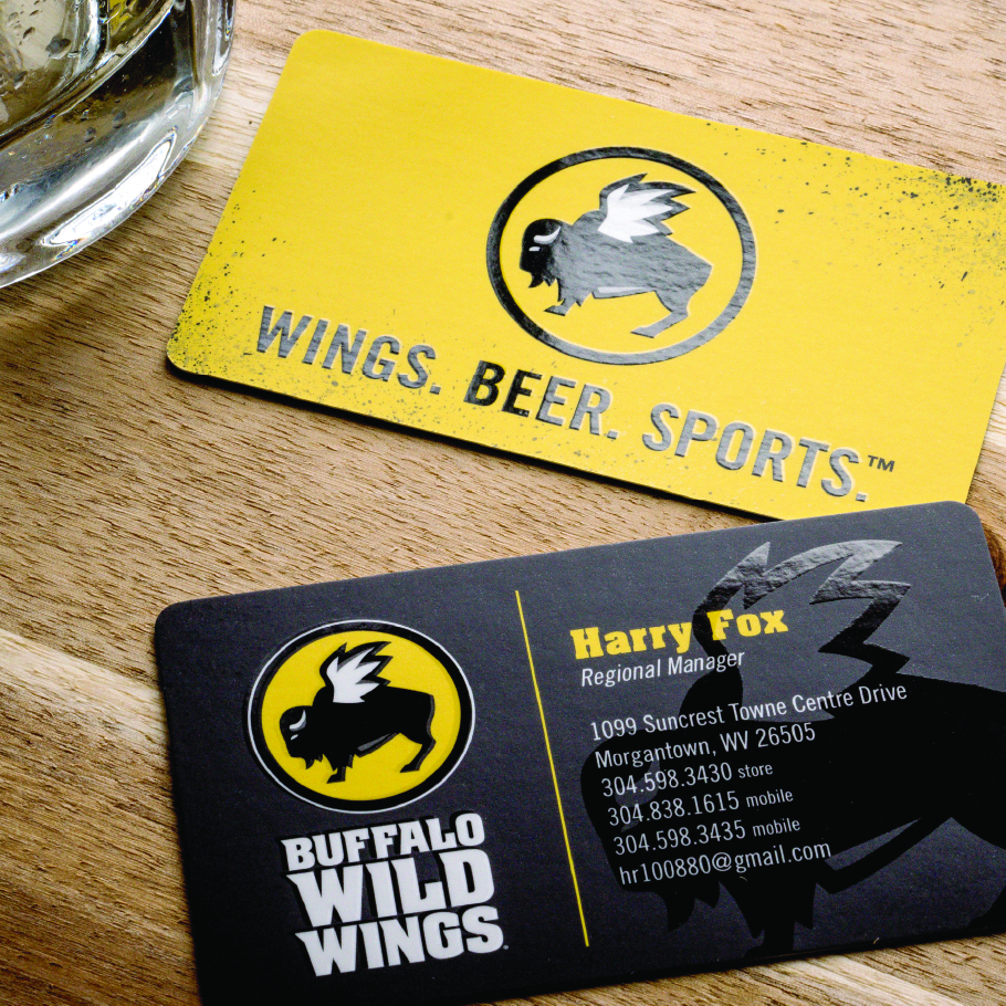 Two Buffalo Wild Wings business cards on a wooden table, one yellow with the logo and slogan 'Wings. Beer. Sports.', and one black showing contact details for Harry Fox, Regional Manager.