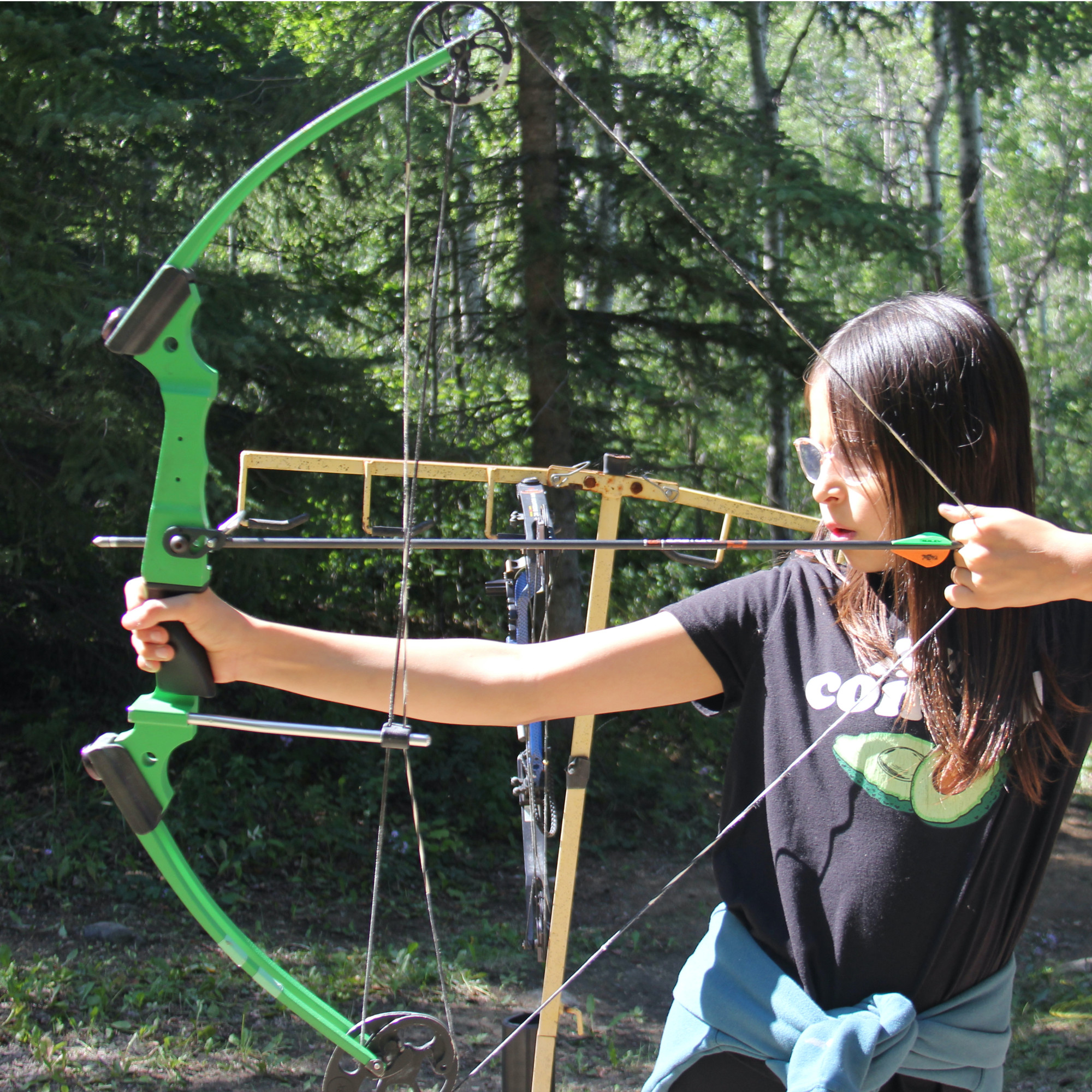 Three campers line up to shoot a bow and arrow.