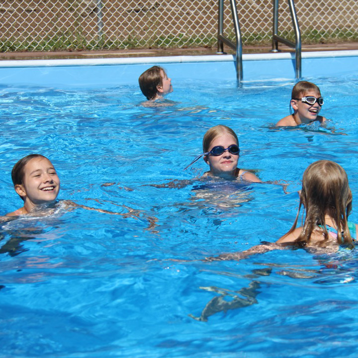 A girl jumps from a diving board while people in the pool watch.