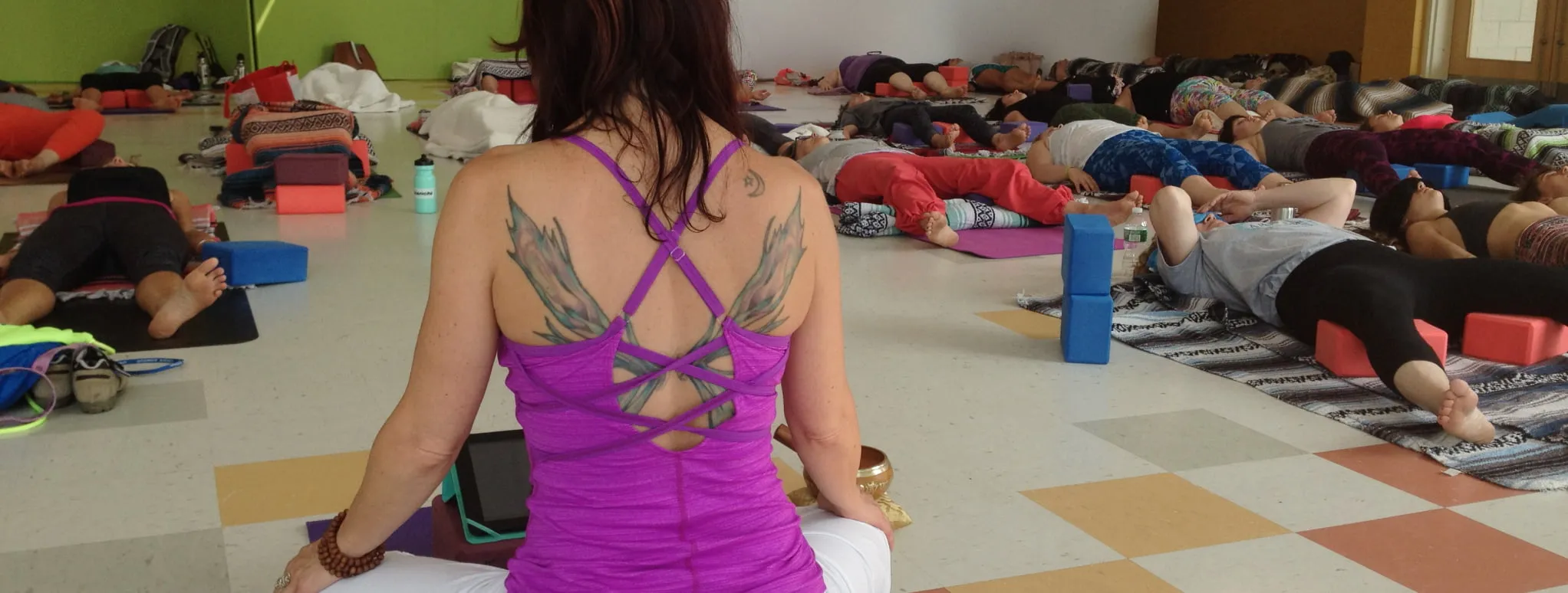 A yoga teacher sitting in front of a group of students lying on their backs with blankets covering them