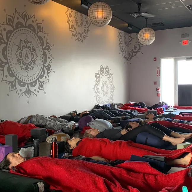 A small group of yoga students lying on their backs with blankets in a yoga studio