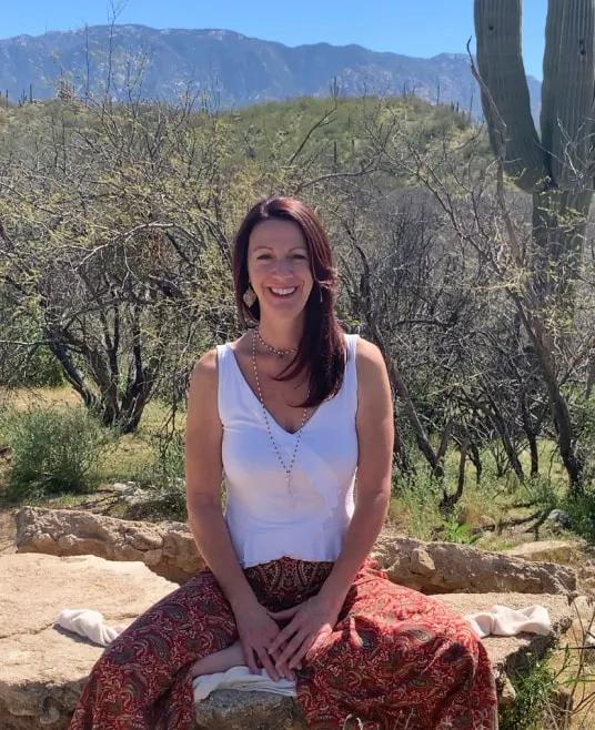 A smiling woman sitting on a large boulder in the desert