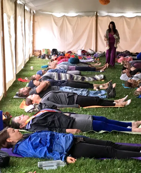 A woman walking in a tent around a group of people lying on yoga mats in a tent