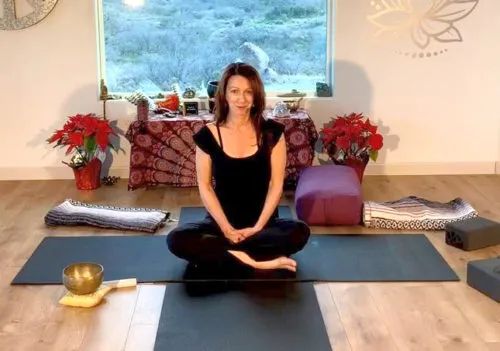 A femal sitting cross-legged on a yoga mat in a yoga studio