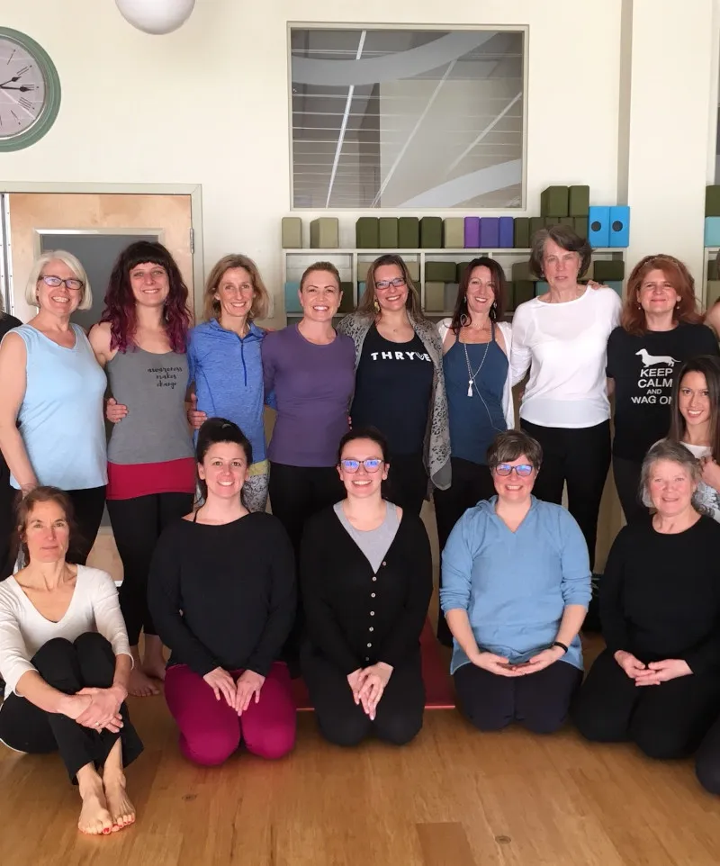 A small group of smiling students sitting together in a yoga studio