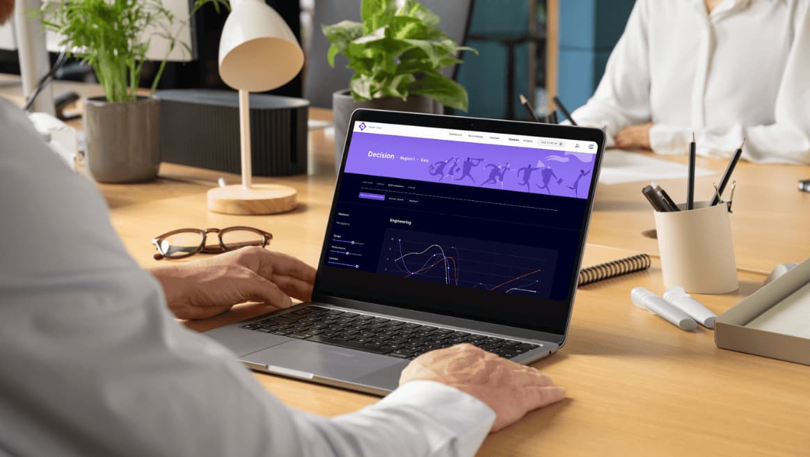 Person using a laptop displaying a data analysis dashboard from the Customer Value Challenge simulation with graphs on a wooden desk with office supplies and plants.
