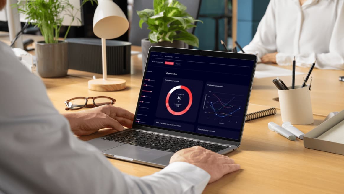 Person working on a laptop displaying the Competitive Advantage data charts at a wooden desk with glasses, plants, and office supplies.