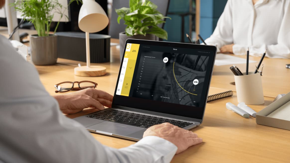 Person working on a laptop displaying a data dashboard of the Business Odyssey Simulation with a tire graphic at a wooden desk in an office setting.