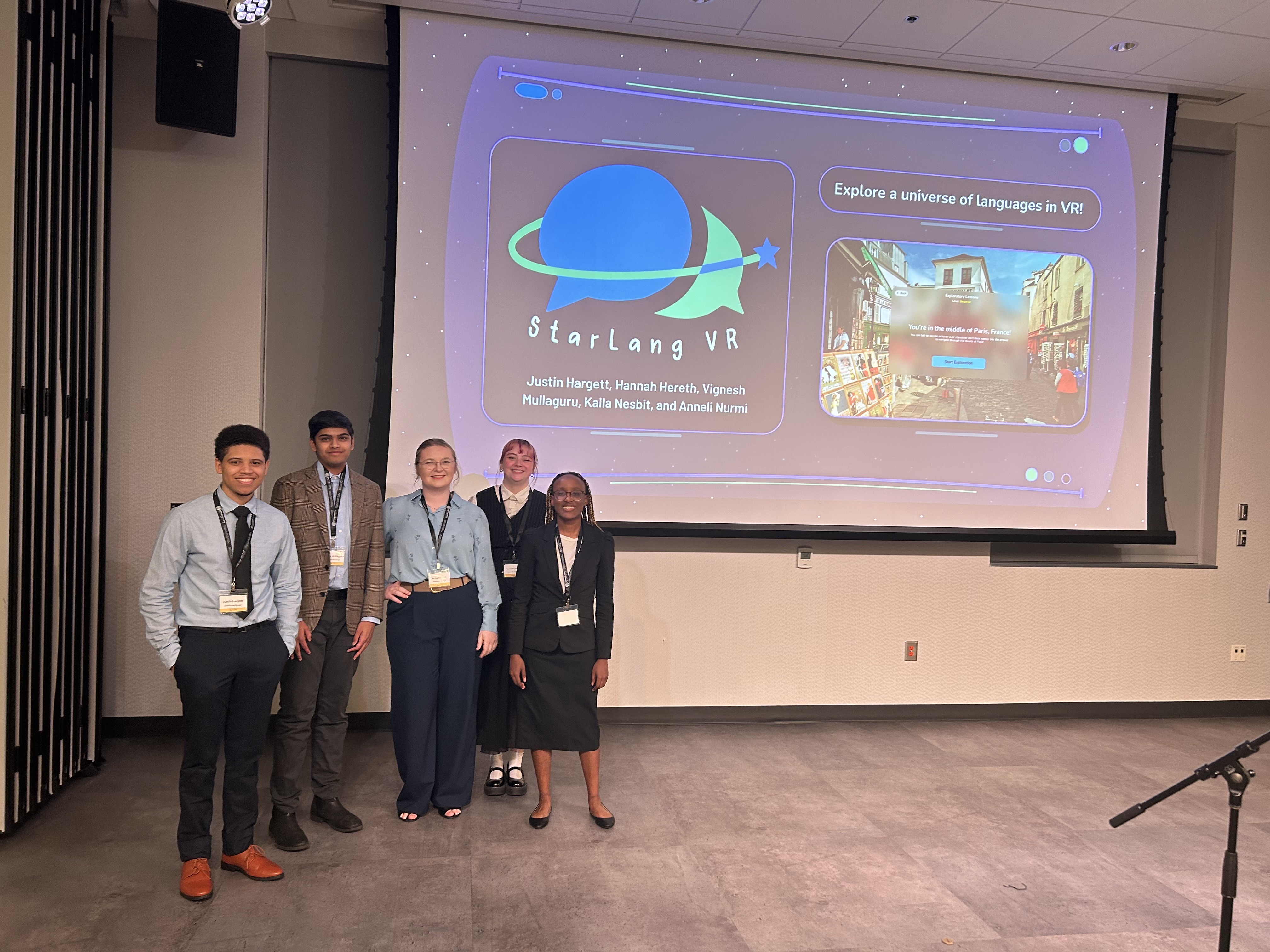 Five people standing in front of a large projected screen displaying 'StarLang VR' presentation with a virtual reality language learning interface.