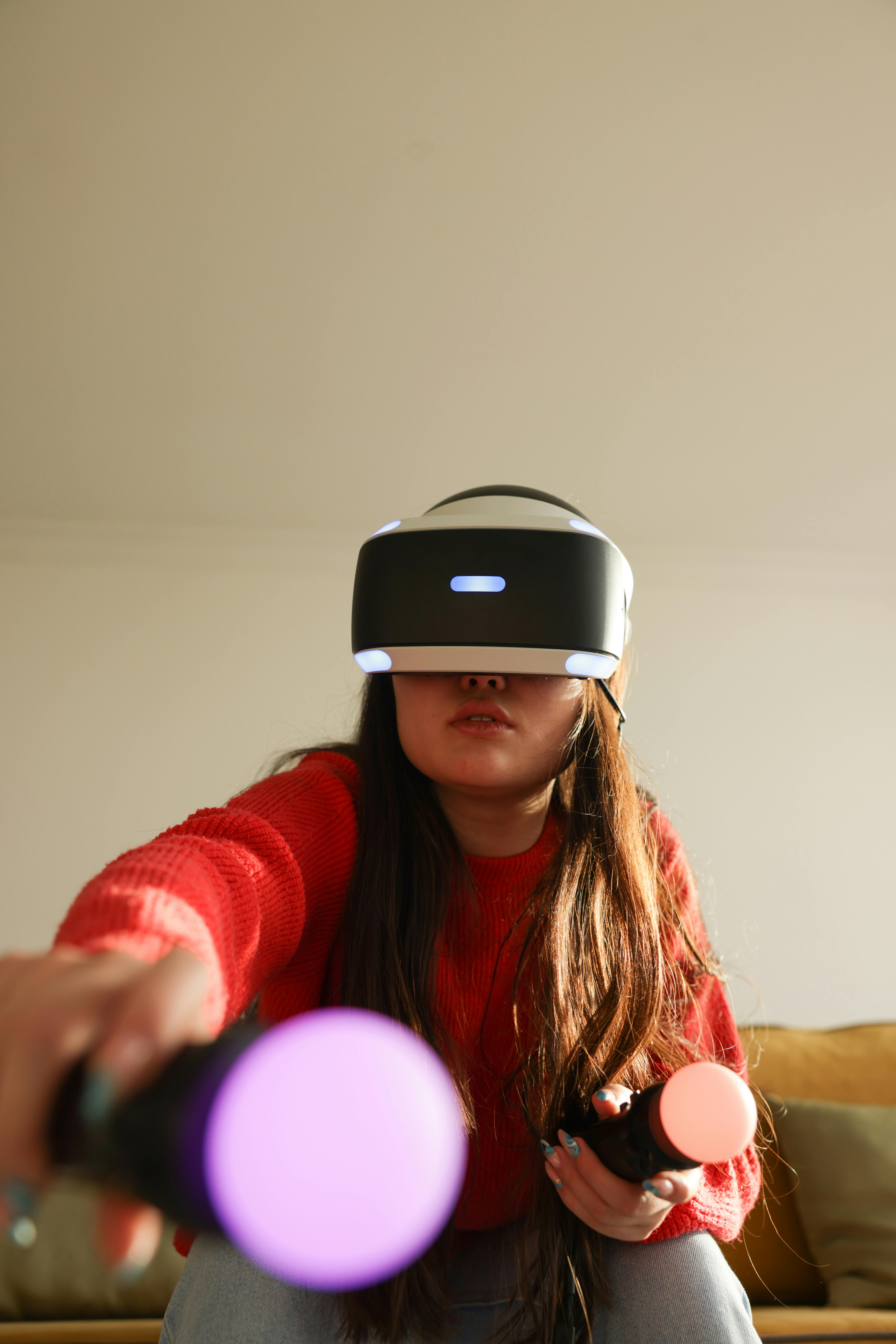 Person wearing a virtual reality headset and holding two glowing motion controllers, playing a VR game indoors.