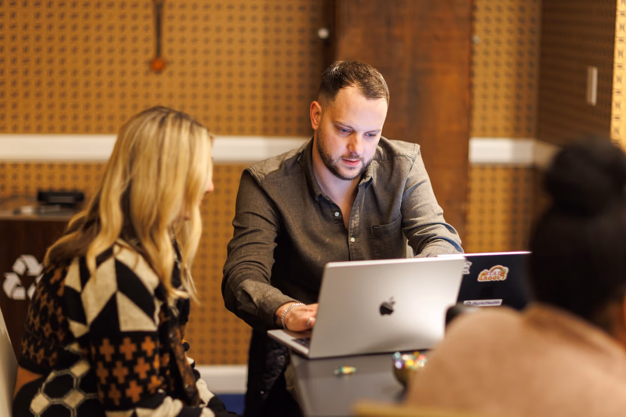 Man and two women working on laptops at a table in a modern workspace.