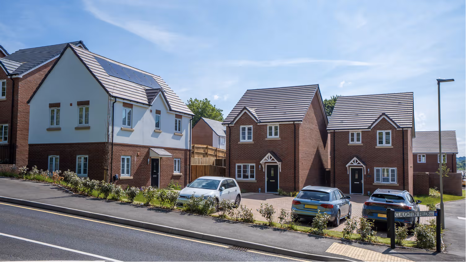 Modern suburban houses with brick and white facades, parked cars, and a street sign labeled Claughton Fields Drive.