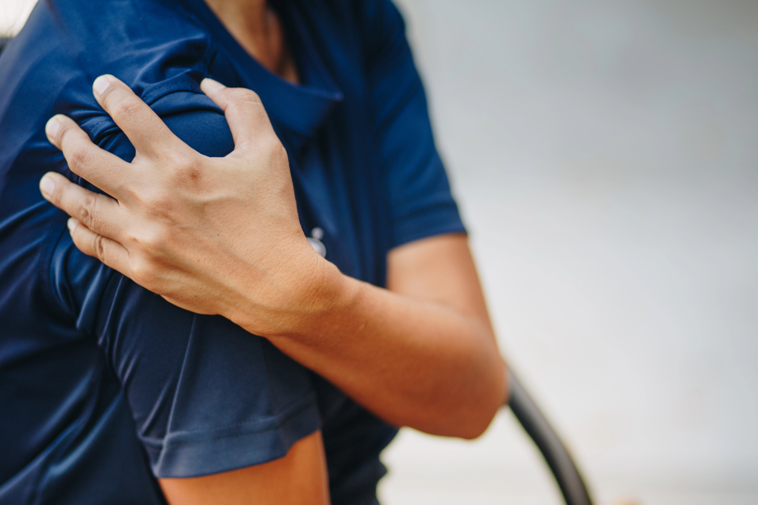 Person in blue shirt holding sore shoulder.