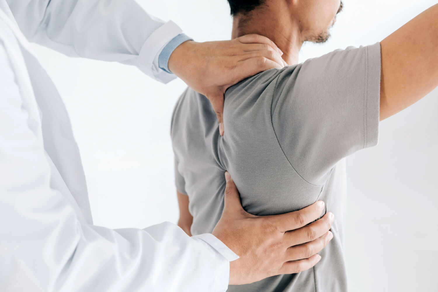 Doctor assessing man's shoulder pain.