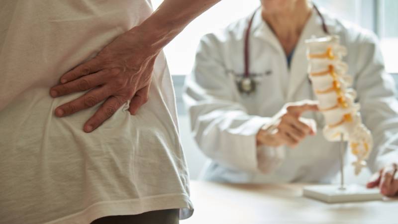 Doctor discusses spine model with patient holding back.