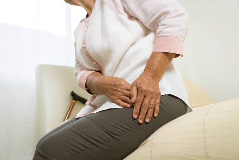 Elderly woman holding hip in pain, cane in background.