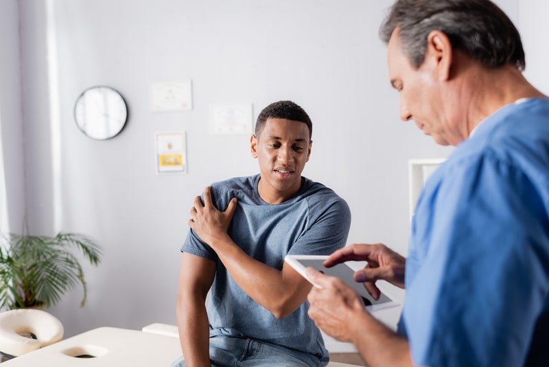 Man holding shoulder talks to doctor in office.