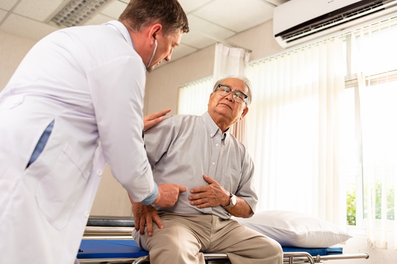 Doctor examines elderly man with abdominal pain.