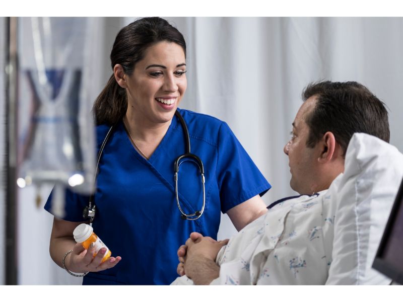 Nurse in blue scrubs giving medicine to male patient in a hospital bed.