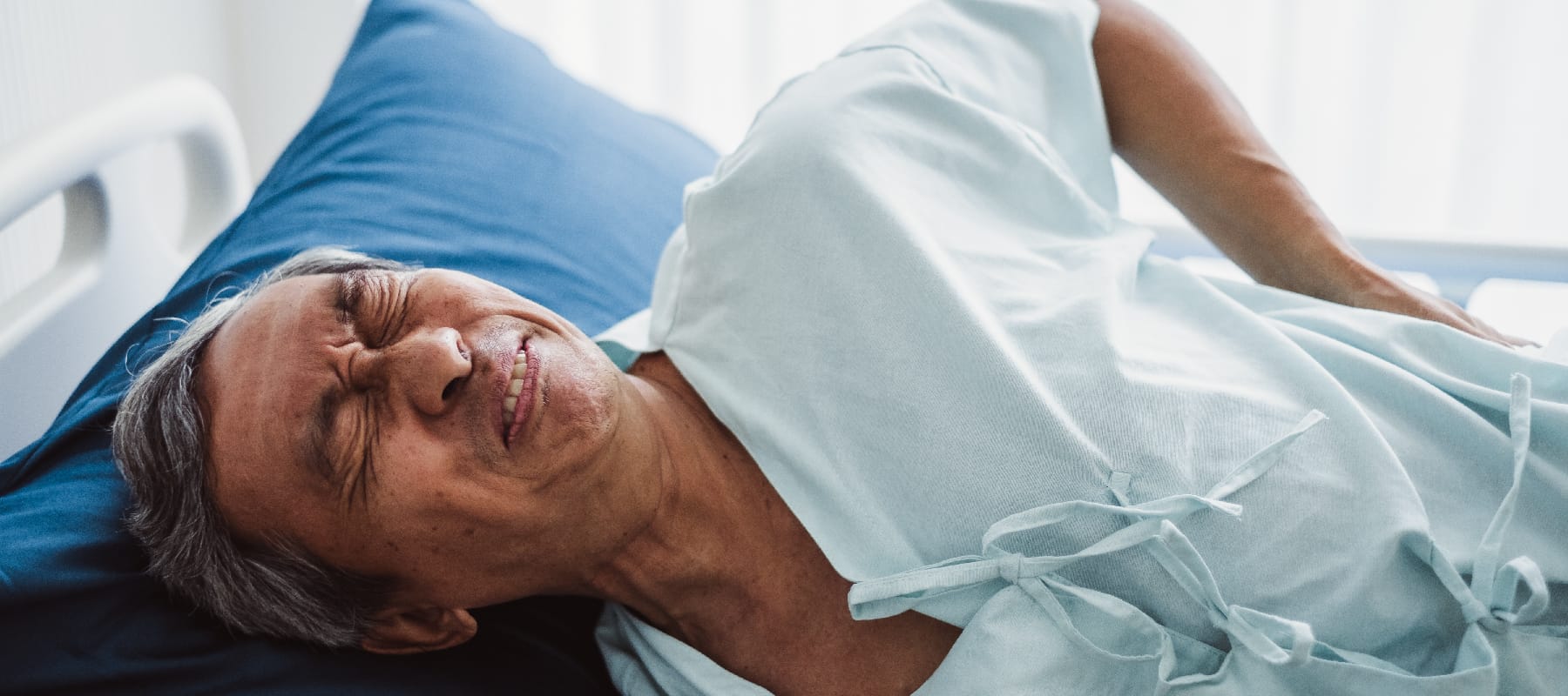 Older man in pain lying in hospital bed.