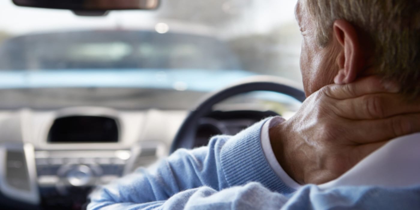 Man in car touching neck in discomfort.