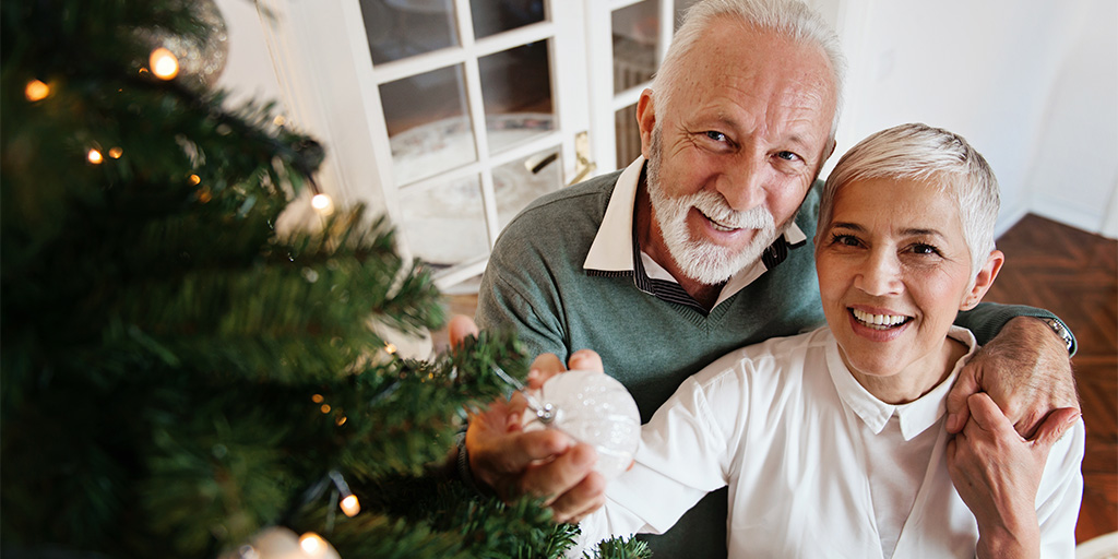 Smiling older couple by Christmas tree.