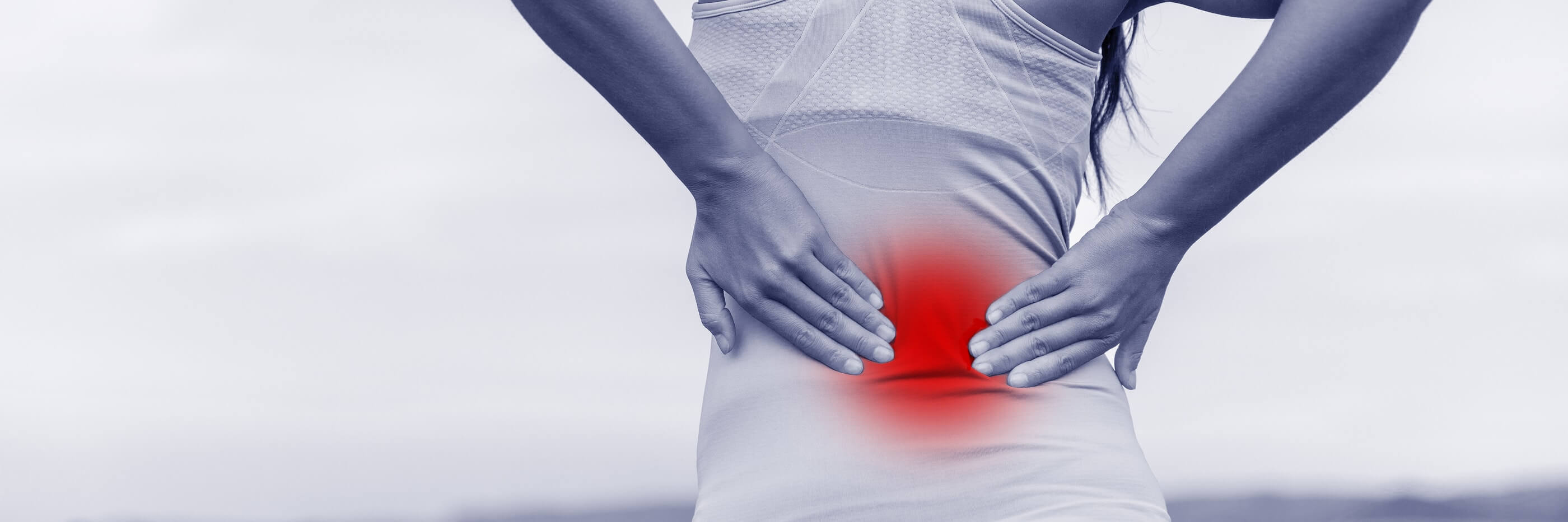 Woman holding lower back in pain, red highlight emphasizes area.