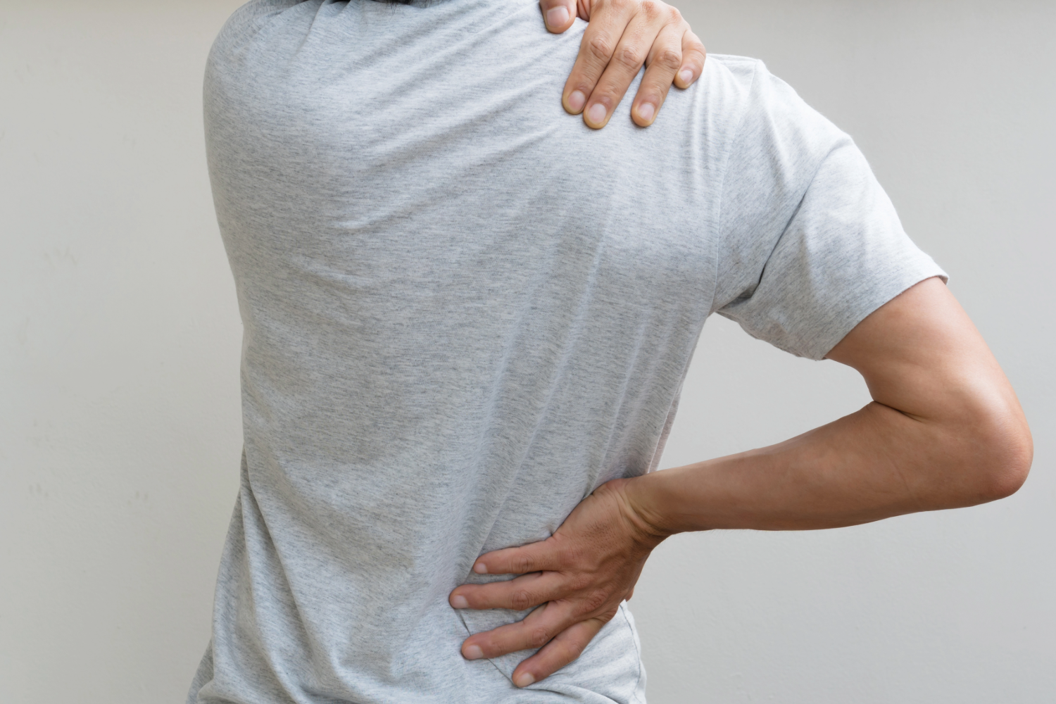 Person in gray shirt holding their back and shoulder in pain.