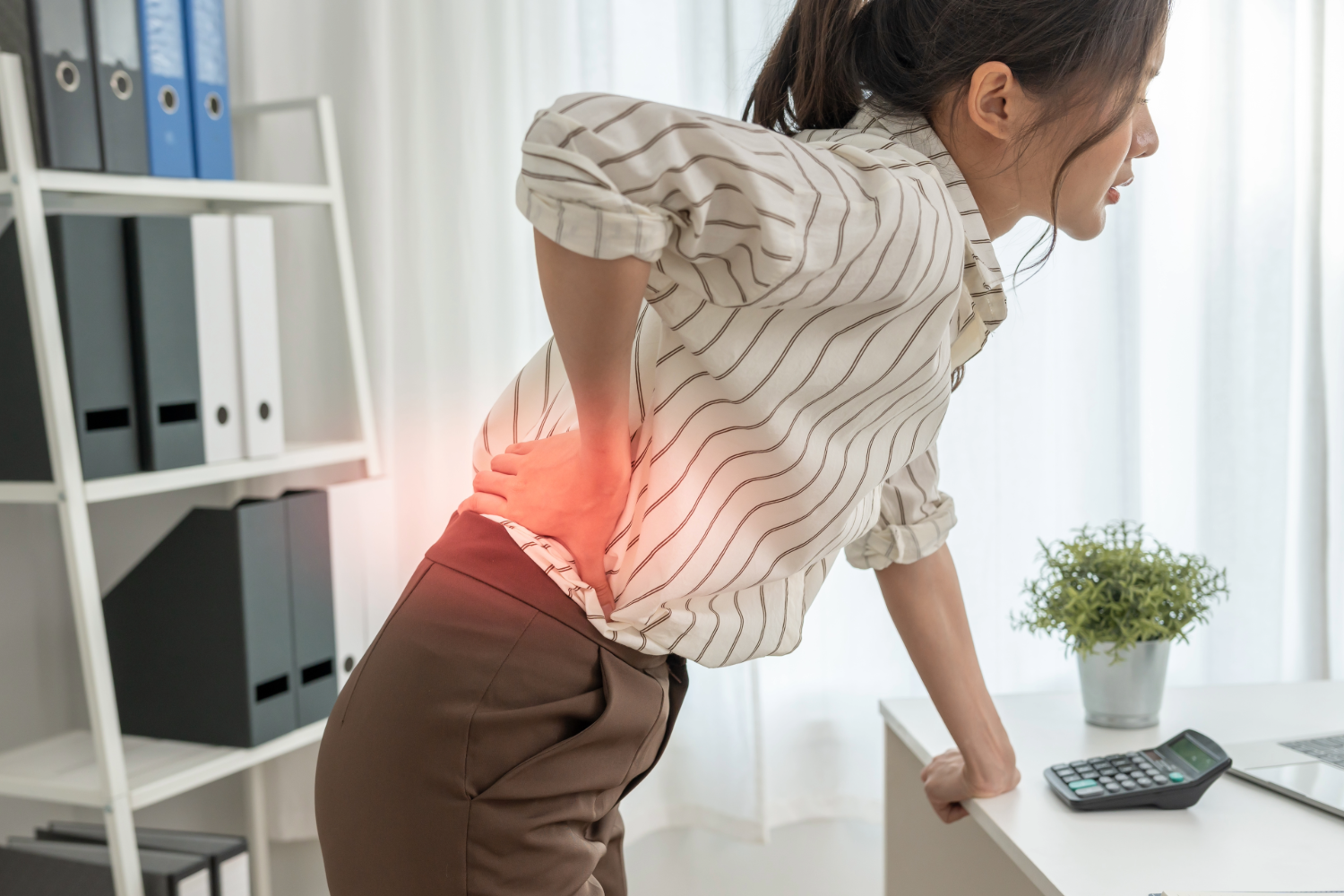 Woman with back pain standing by desk in office.