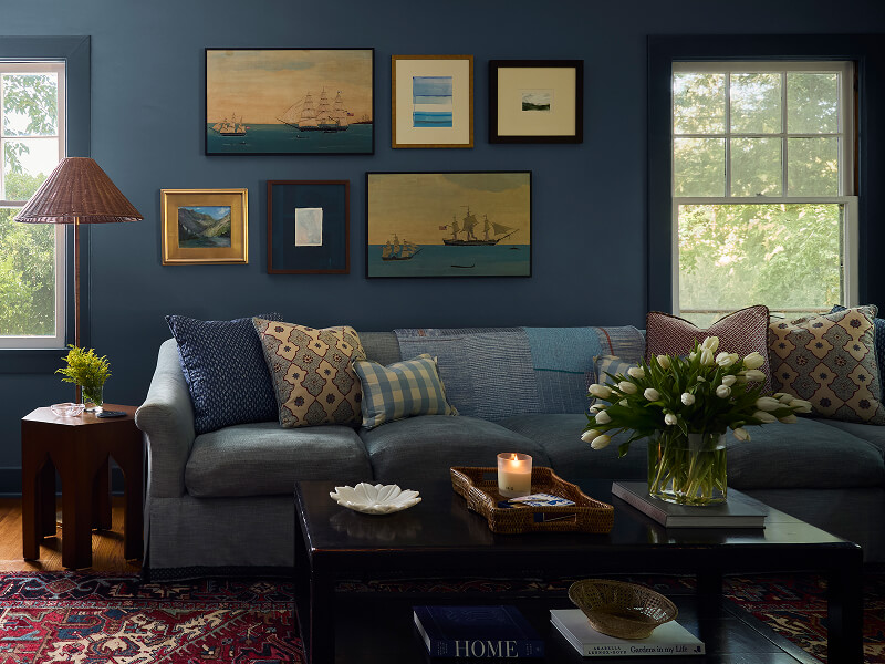 Cozy living room with blue walls, sofa with patterned pillows, framed art, vase with white tulips.