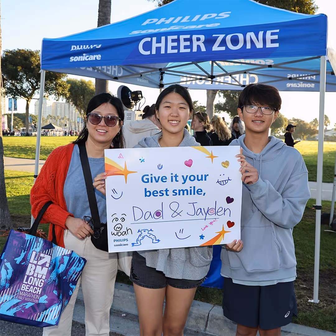 Three people holding a sign beside a tent