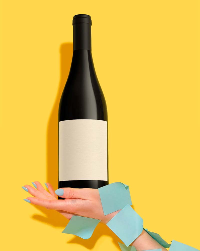 hand covered with blue post-it holding a bottle of wine on a yellow background