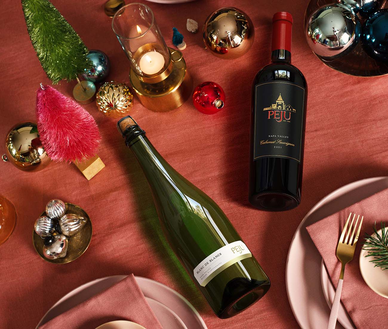 PEJU Cabernet Sauvignon and sparkling Blanc de Blancs displayed on a festive holiday table with ornaments, candles, and place settings.