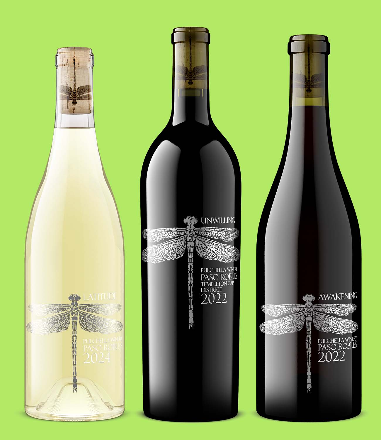 Three Pulchella Winery bottles—Latitude white wine, Unwilling red wine, and Awakening red blend—featuring a detailed dragonfly illustration on a clean green background.
