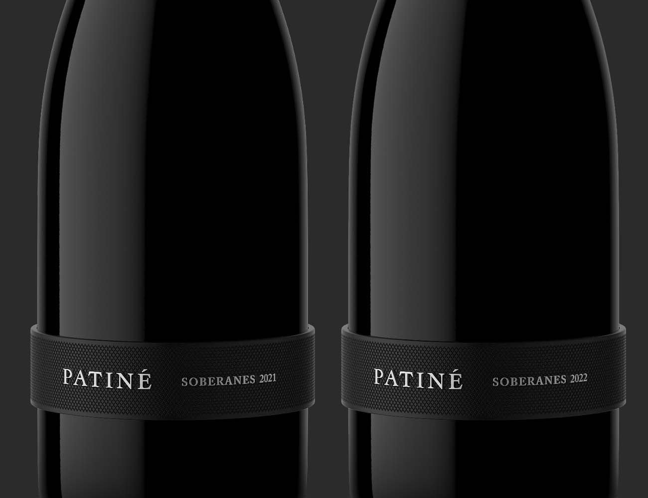 Close crop of two dark wine bottles highlighting label embossing, label texture, and premium packaging details.