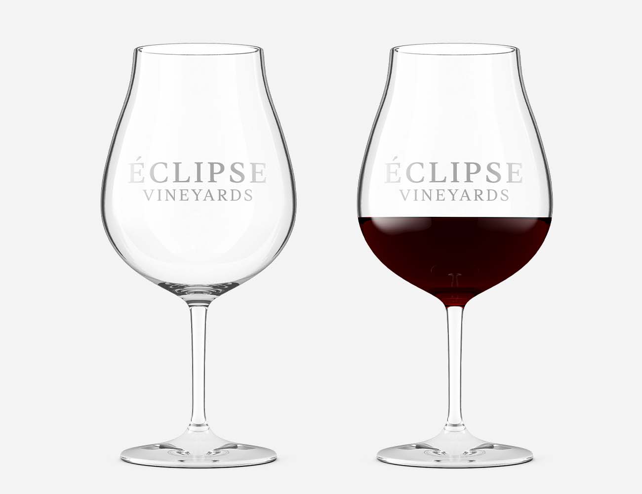 empty wine glasses with etched winery logo, next to the same wine glass with medium-bodied red wine