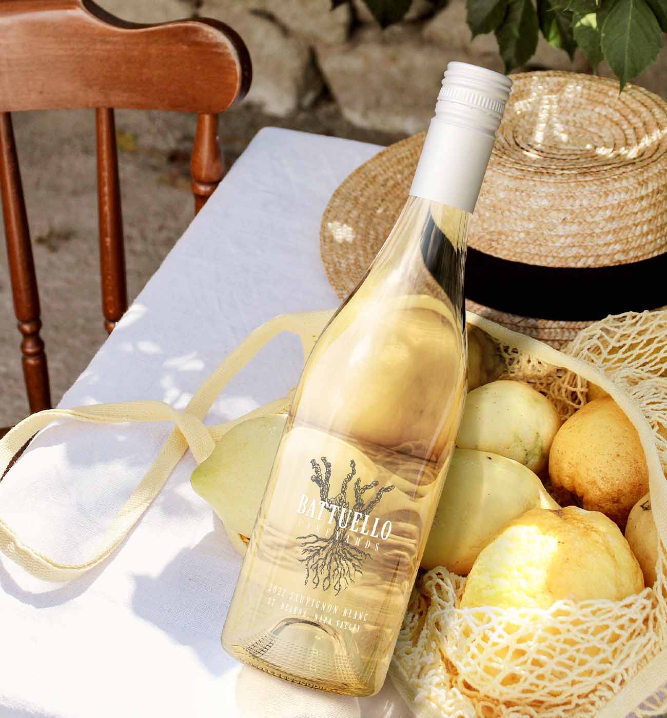 silk printed bottle of sauvignon blanc leaning on a bag lemon with a summer hat on an outdoor table on a sunny day