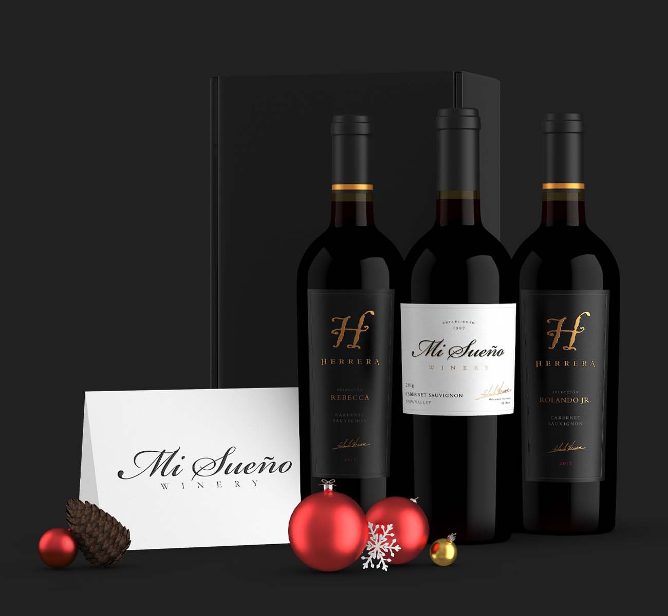 3 wine bottles in front of a gift box next to a card and Christmas ornaments