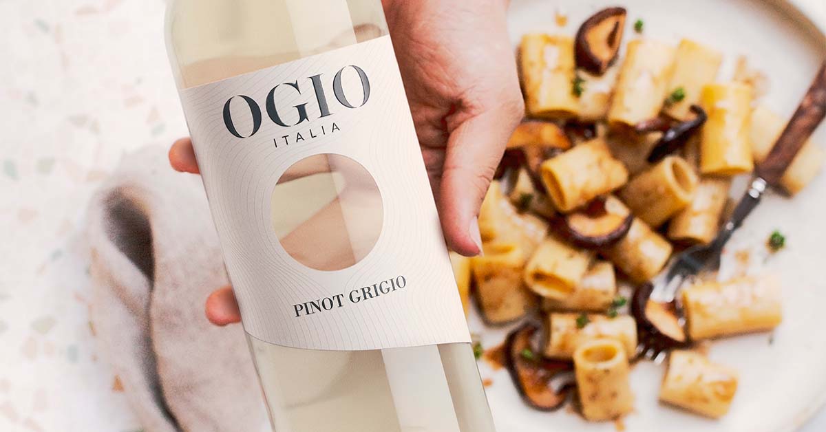 Modern wine packaging with OGIO wine bottle held in hand above a table in a lifestyle food pairing scene