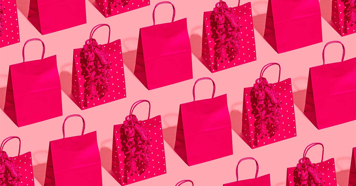 red paper gift bags lined up on a pink background