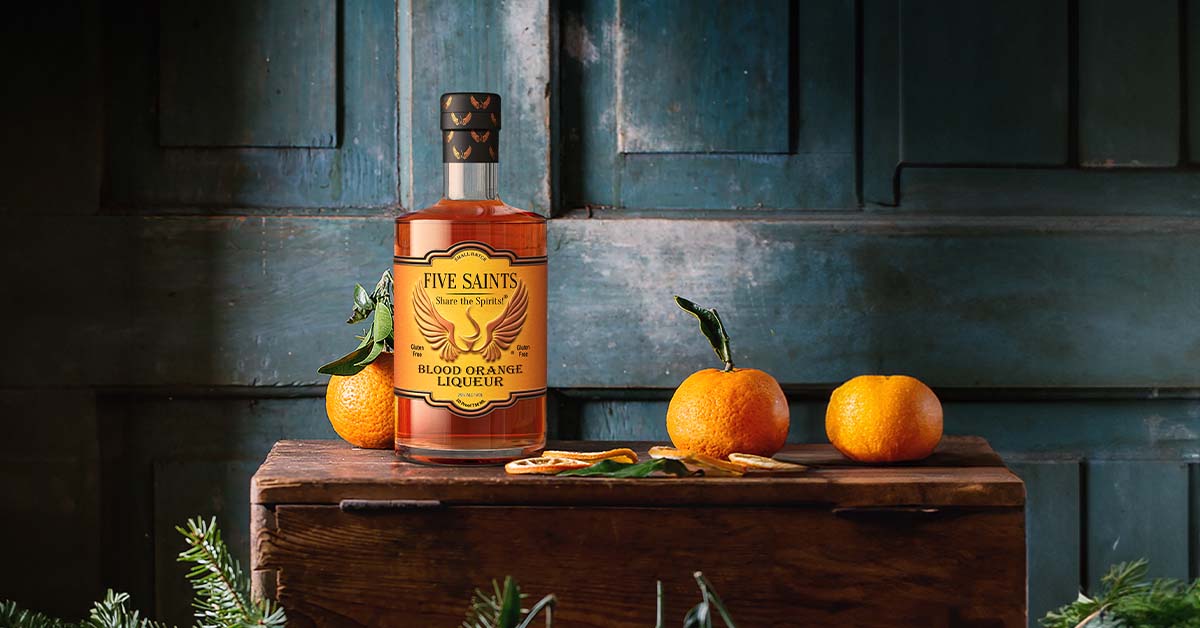 lifestyle campaign image of a blood orange liqueur bottle on a wood chest with oranges