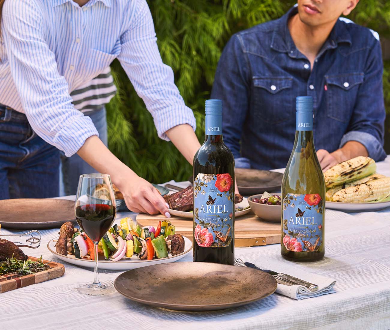 Ariel non-alcoholic Cabernet Sauvignon and Chardonnay bottles at an outdoor dinner, lifestyle wine product photography with grilled food