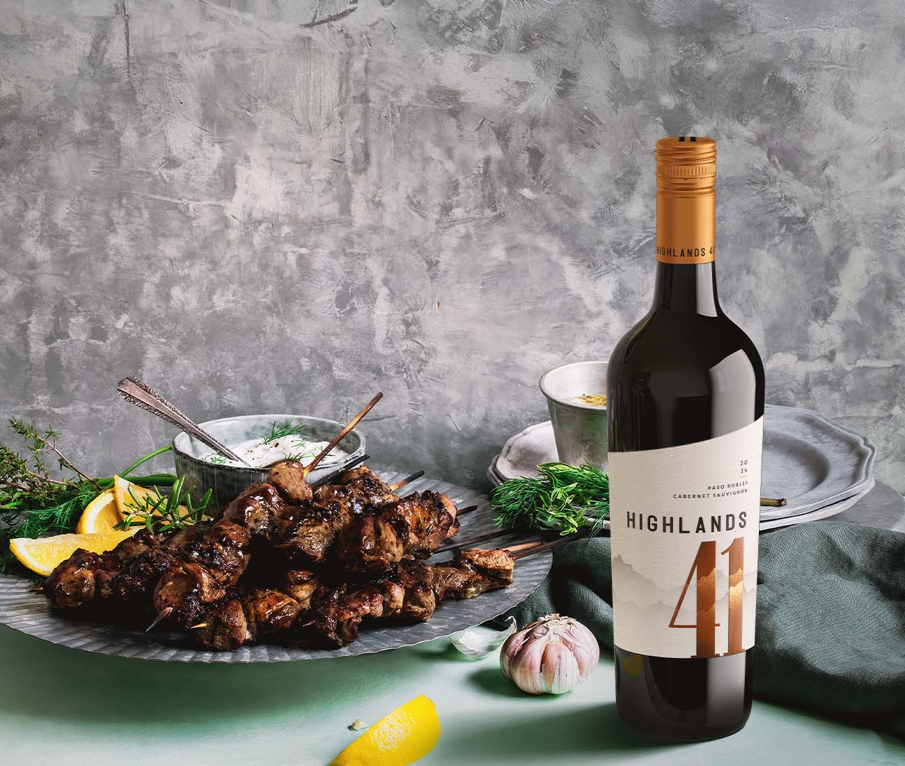 Bottle of Paso Robles Cabernet Sauvignon next to Greek chicken skewers, recipe image from Outshinery