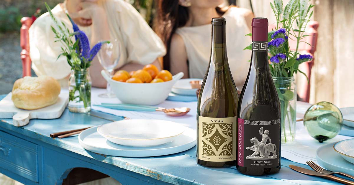 lifestyle image by Outshinery where a bottle of pinot noir and a bottle of chardonnay are on a table outdoor with people in the background